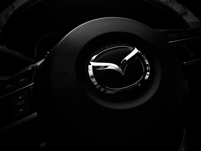 A steering wheel with the Mazda logo in the center of it, set against a black background.